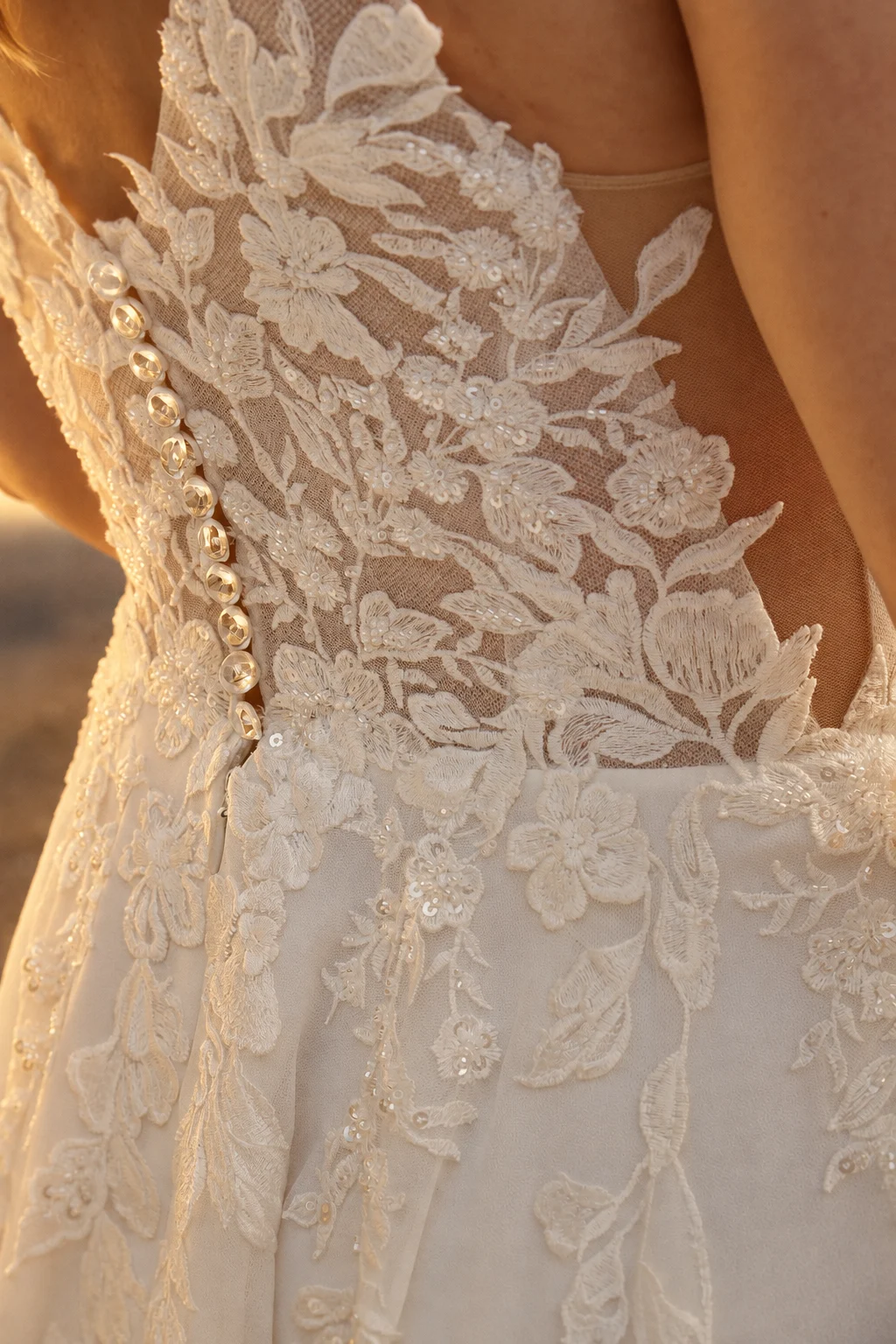 Détail de dentelle florale et de boutons nacrés sur une robe de mariée