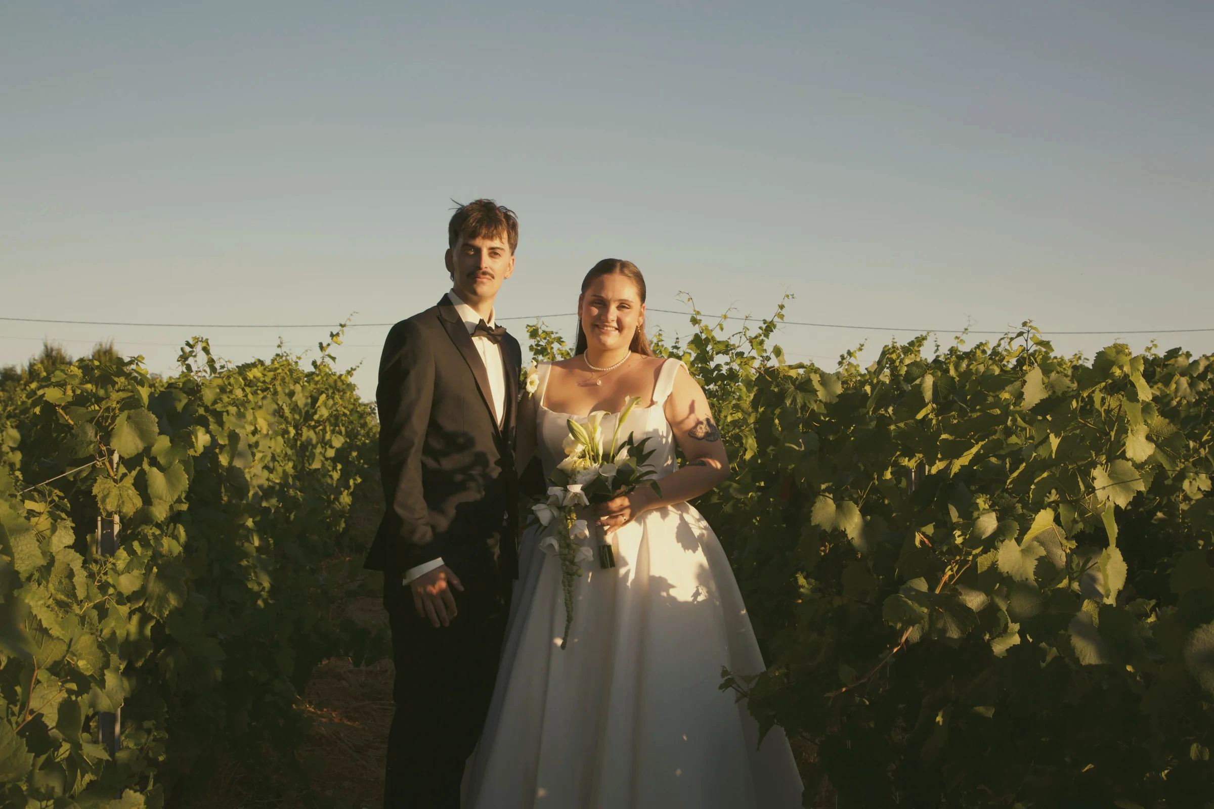 Les mariés marchent entre les rangs de vigne dans la lumière dorée